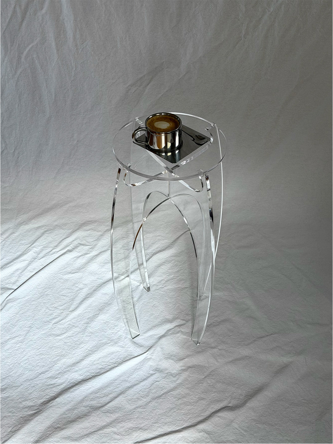 Aer Table transparent acrylic side table styled with an espresso cup and saucer on its circular top, shown against a white linen backdrop