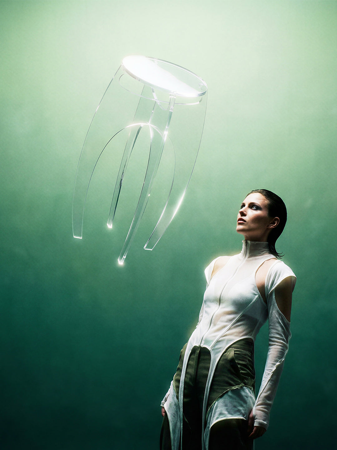 Editorial campaign image of the Aer Table clear acrylic side table appearing to levitate above a model in a teal atmospheric setting
