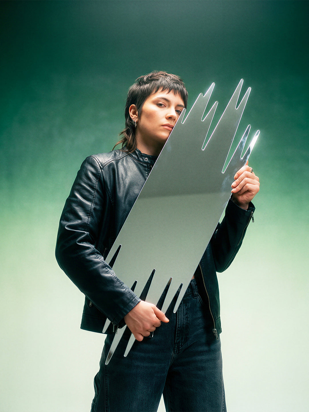 Person holding a large, metallic, spike-like object against a gradient green background
