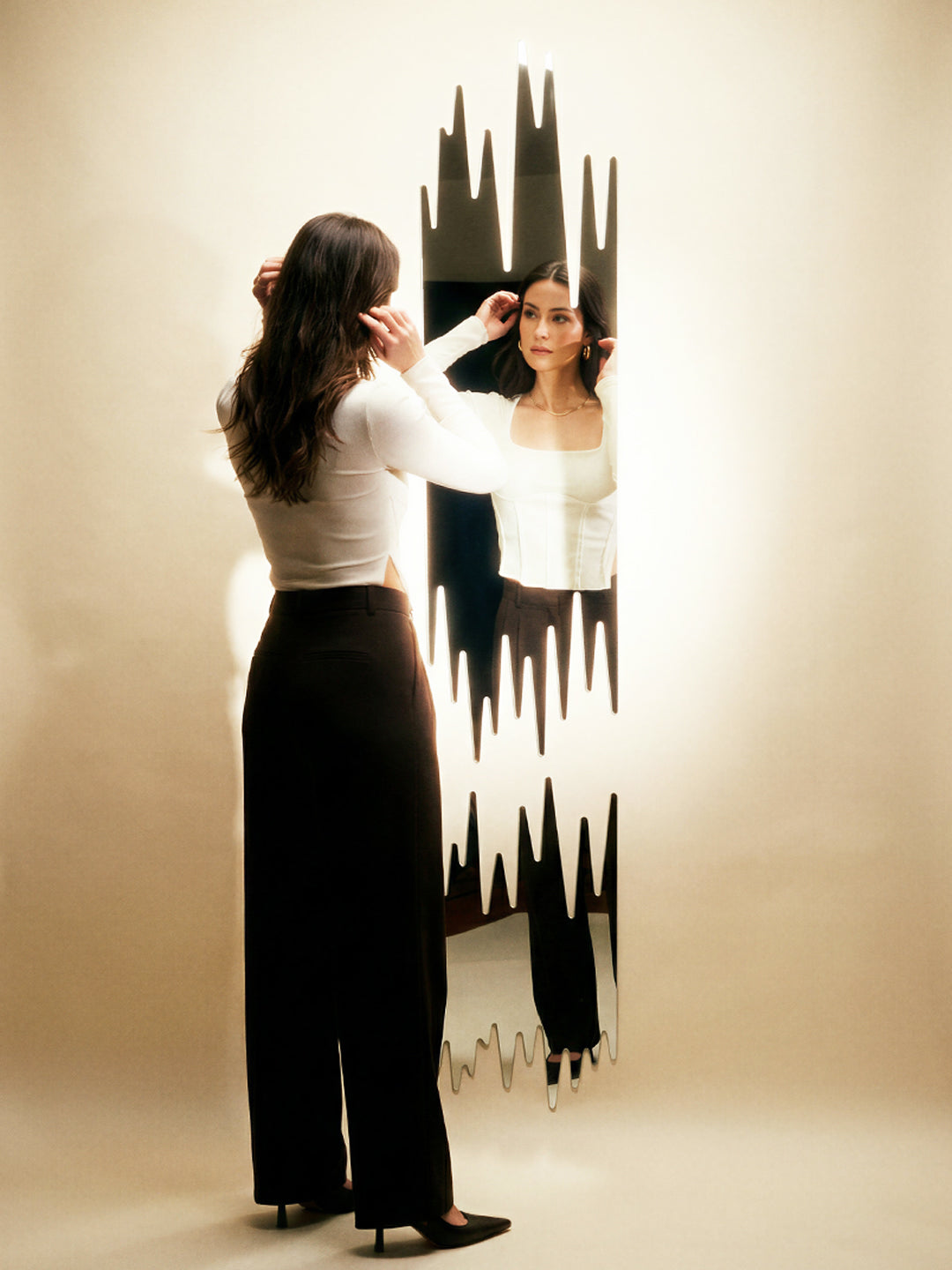 Woman adjusting an earring in front of Mirror 001, full-length spiked-edge mirror in a studio setting