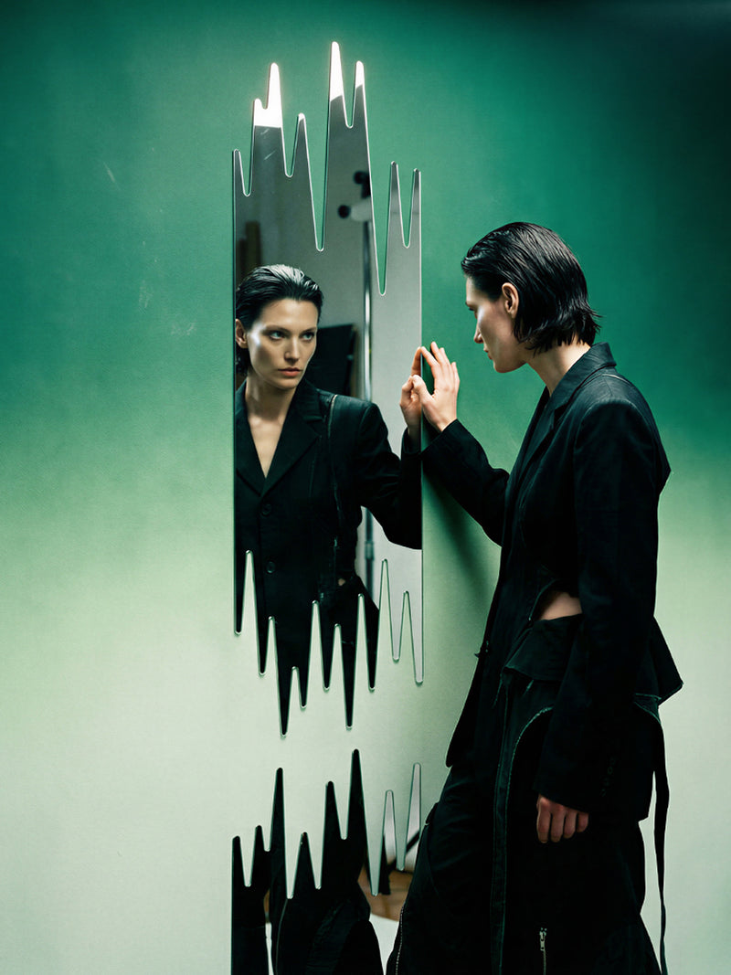 Person in a black outfit interacting with a futuristic mirror on a green 
