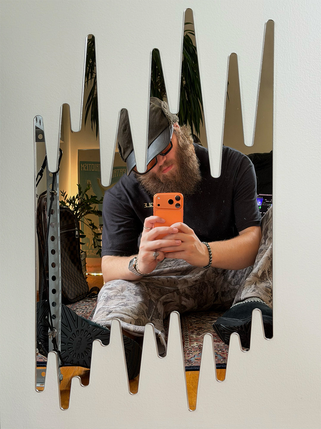 A man with a beard and cap taking a mirror selfie in a home setting, with a uniquely shaped zigzag mirror reflecting his figure and the room behind him.