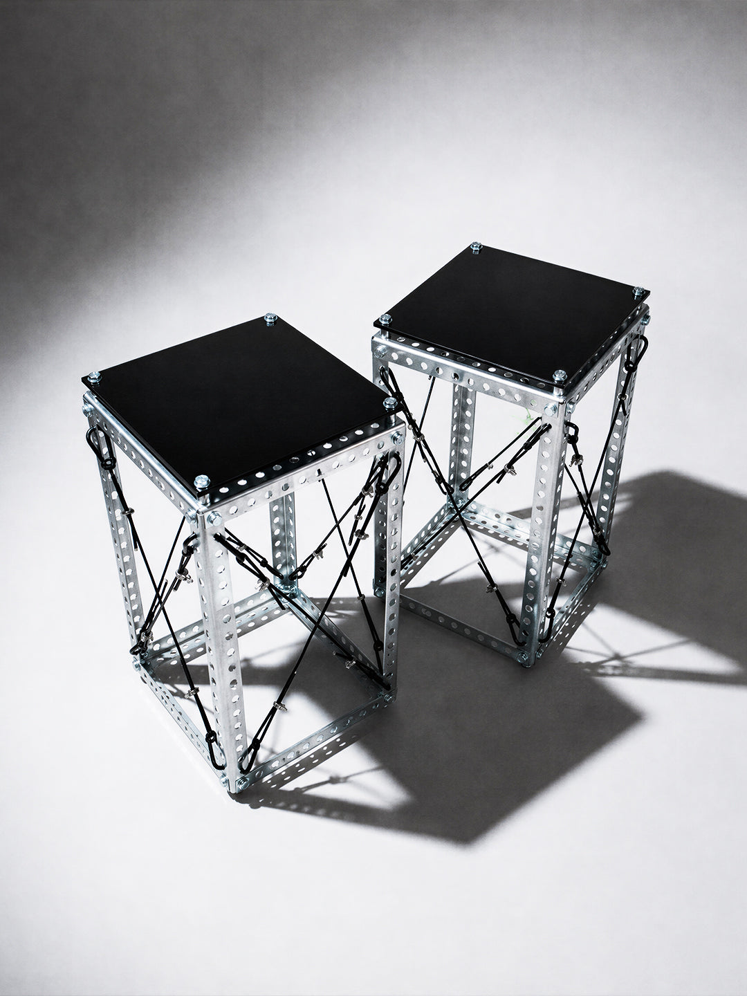 Side Table Set DP-001 pair shown at an angle, revealing the Diagrid steel frame's crossed cable bracing and black tabletops
